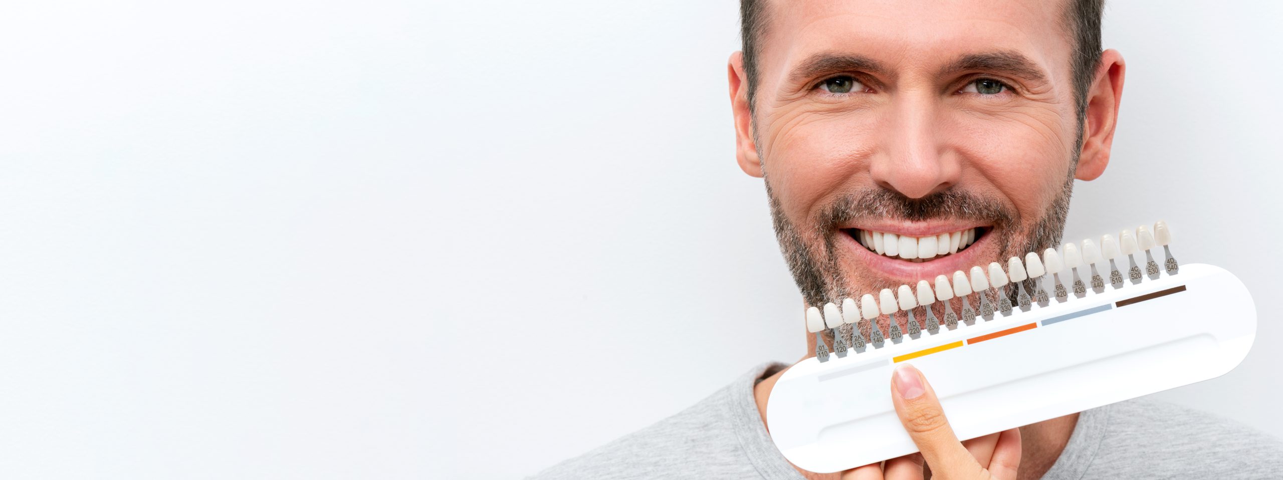 Tooth whitening, white perfect smile. Smiling man with whitening shade guide